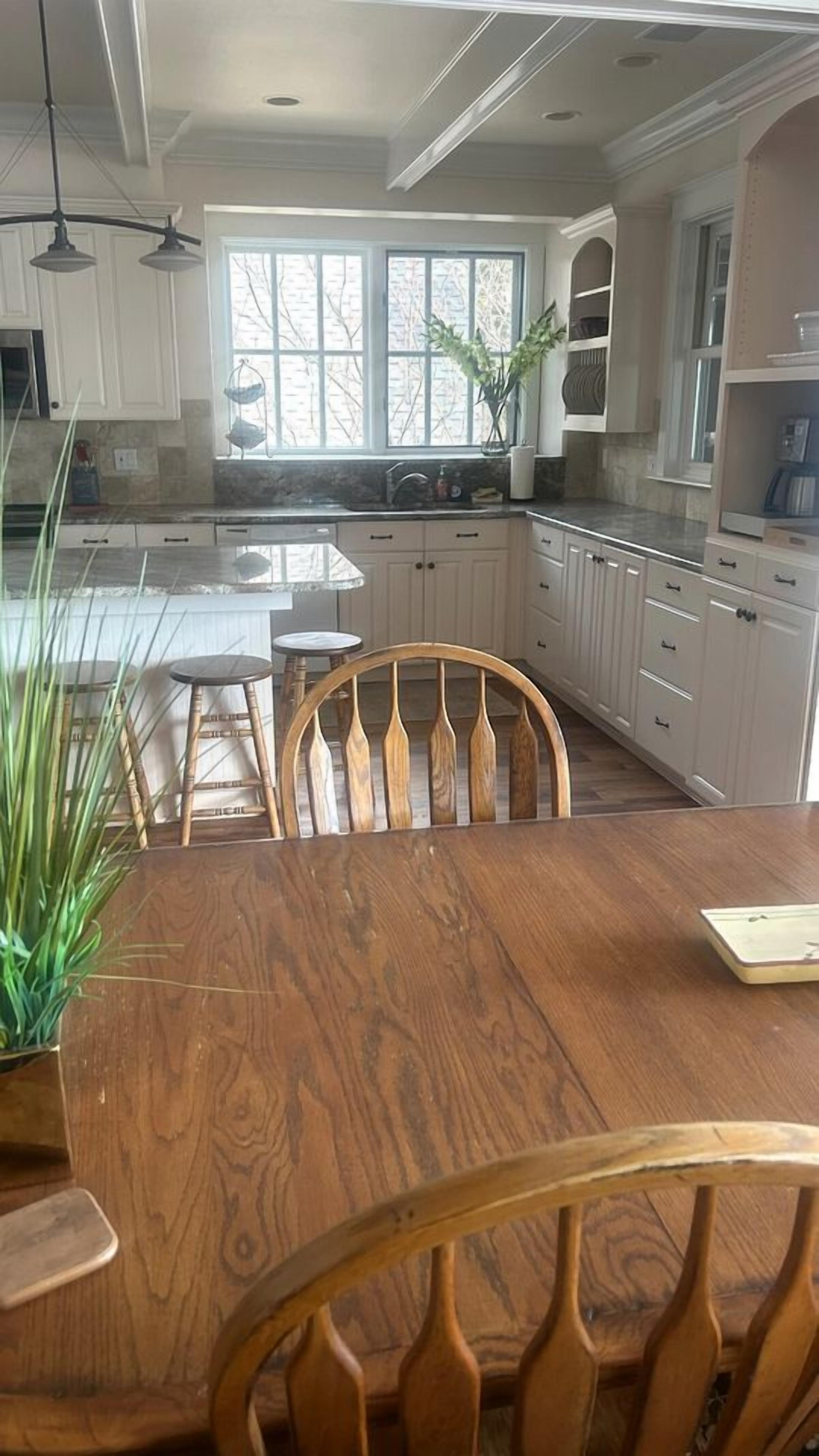 A kitchen with white cabinets, a wooden dining table, and a window.