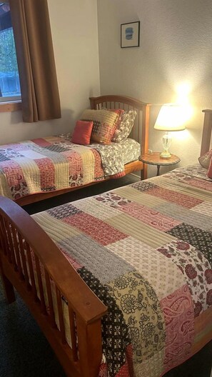 A hotel room with two single beds, a bedside table with a lamp, a window with curtains, and a framed picture on the wall. - Peaceful Waterfront Retreat with Fire Pit & Nature-Filled Surroundings in McCall, Idaho (McCall)
