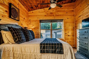 Quarto de cabana de madeira com cama, almofadas, cómoda e ventoinha no teto.