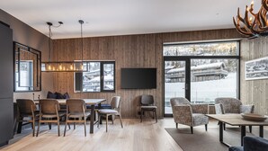 A modern interior with a dining area, seating, a flat-screen TV, and large windows with a snowy view.