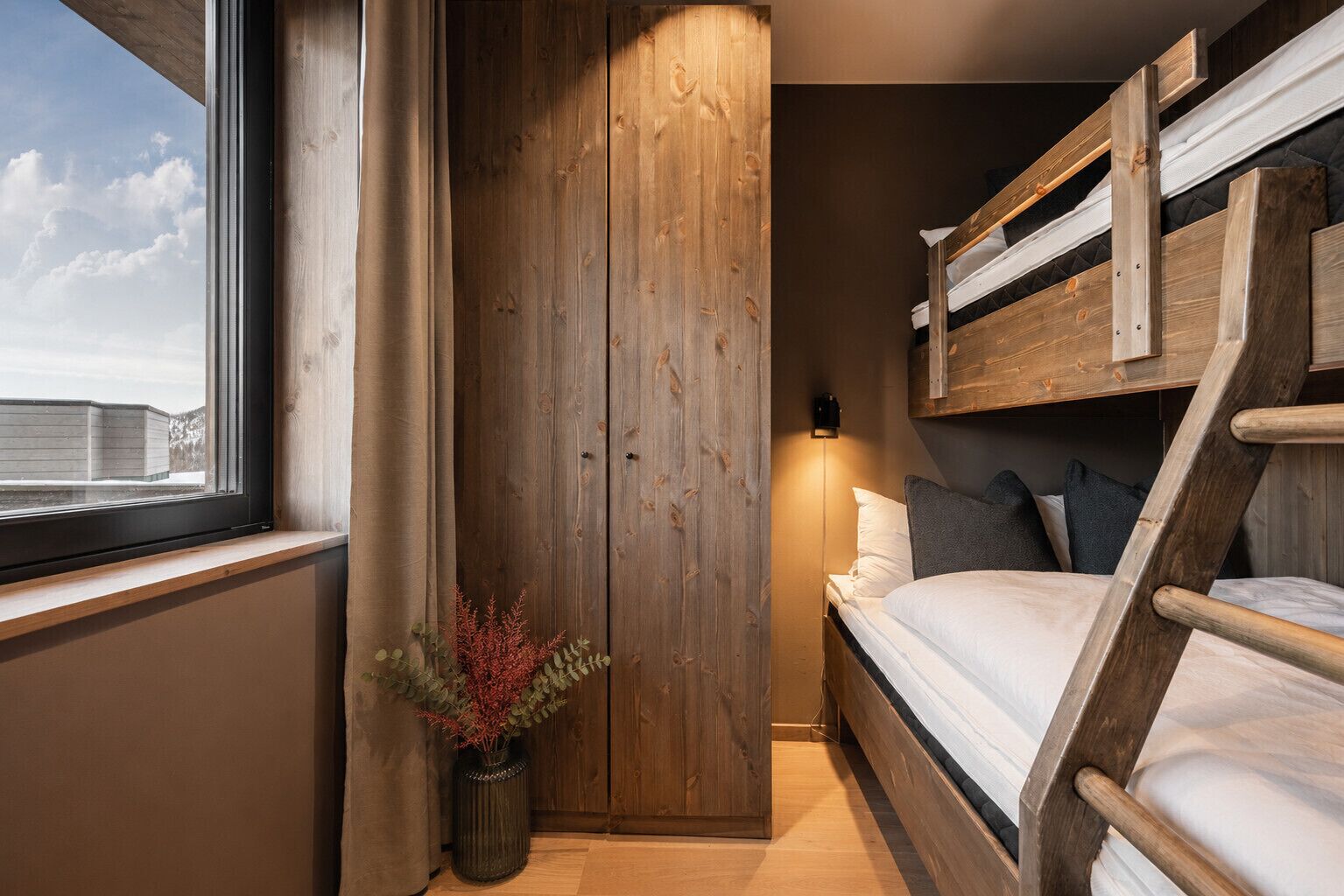 Quarto com beliche, guarda-roupa de madeira e luminária de cabeceira.