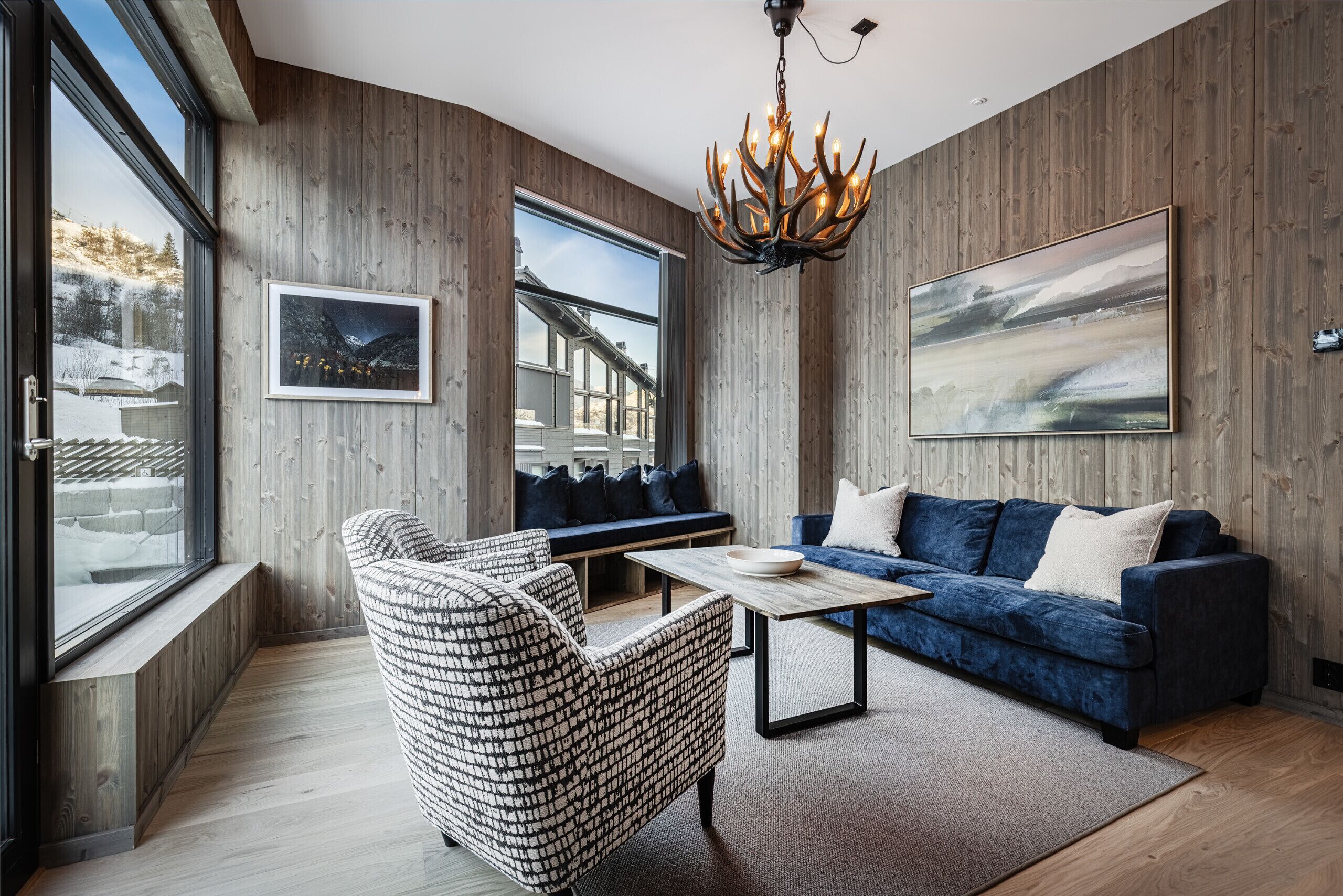 Una sala moderna con un sofá azul, un sillón estampado y una pared de madera decorativa.
