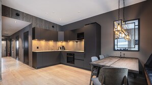 A modern kitchen with dark cabinetry, a wooden dining table, and a hanging light fixture.
