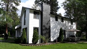 Une maison à deux étages avec une cheminée en briques, un revêtement extérieur blanc et une terrasse aménagée avec du mobilier d’extérieur.