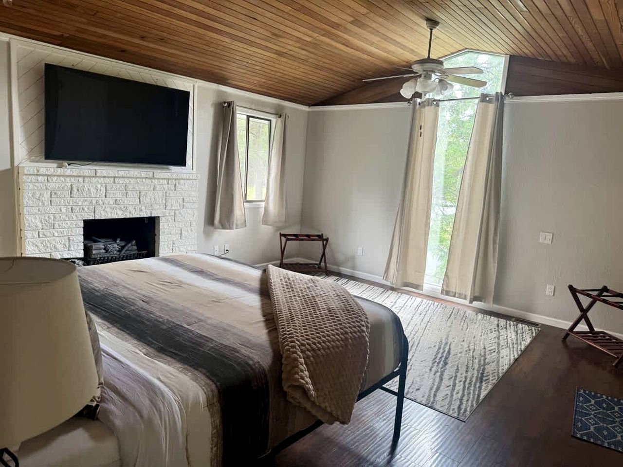 A bedroom with a fireplace, a bed, a TV, and a window with curtains.