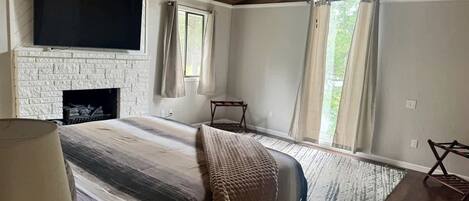 A bedroom with a fireplace, a bed, a TV, and a window with curtains.
