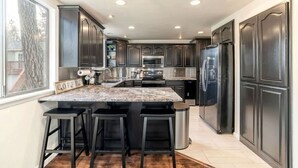 A modern kitchen with dark cabinets, a granite countertop, stainless steel appliances, and a bar stool area. - Vacation Home with Private Court & Entertainment Space in Post Falls, Idaho (Post Falls)