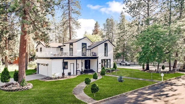 A two-story house with a balcony, surrounded by trees and a well-maintained lawn. - Vacation Home with Private Court & Entertainment Space in Post Falls, Idaho (Post Falls)