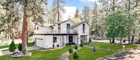 A two-story house with a balcony, surrounded by trees and a well-maintained lawn.