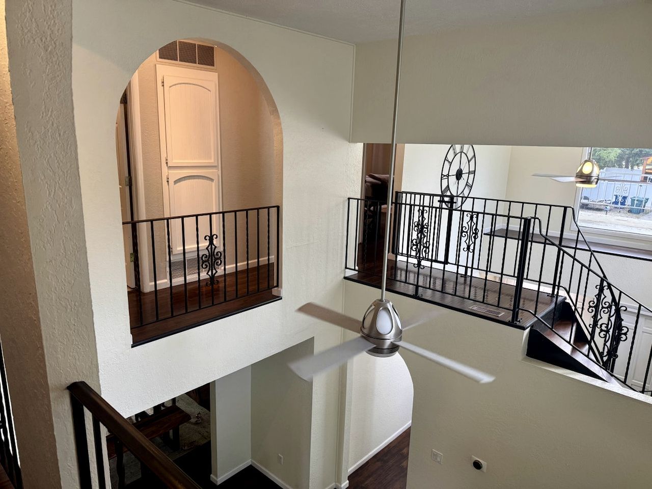Un interior de varios niveles con una escalera, un ventilador de techo y una ventana con barandilla de metal decorativa.