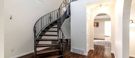 A spiral staircase with a metal railing, wooden steps, and a white wall.