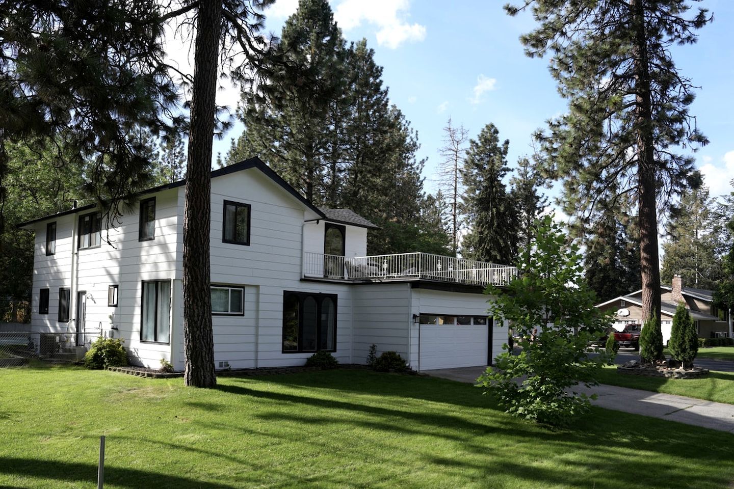 A two-story white house with a balcony, surrounded by tall trees and a well-maintained lawn.