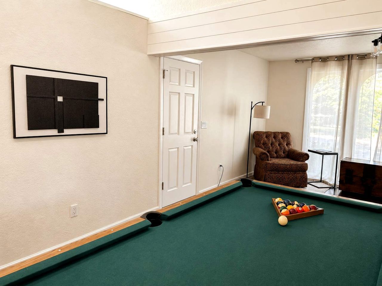 A pool table with balls, a door, a chair, and a lamp.