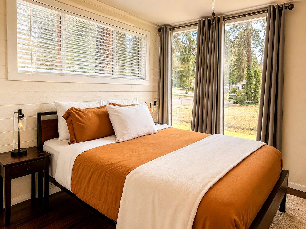 Un dormitorio con una cama grande, una mesita de noche, una lámpara y una ventana con cortinas.