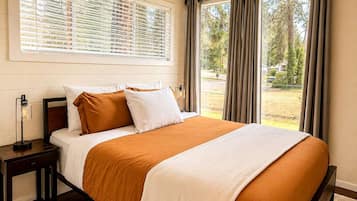 Un dormitorio con una cama grande, una mesita de noche, una lámpara y una ventana con cortinas.