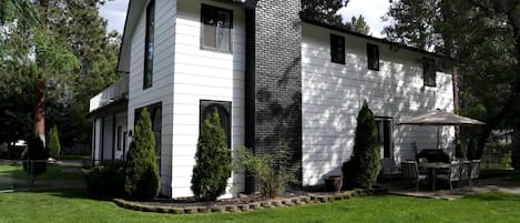 A two-story house with a brick chimney, white siding, and a patio with outdoor furniture.