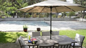 Une terrasse extérieure avec une table et des chaises, un grand parasol et une piscine en arrière-plan.