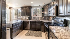 A modern kitchen with dark cabinetry, stainless steel appliances, and a granite countertop. - Vacation Home with Private Court & Entertainment Space in Post Falls, Idaho (Post Falls)