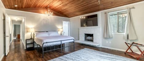 A bedroom with a bed, a fireplace, a ceiling fan, and a view of the outdoors.