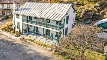 A two-story building with a balcony, a porch with outdoor seating, and a stone foundation.