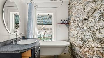 Ein Badezimmer mit einer Badewanne, einem runden Spiegel, einem Fenster mit Blick und einer Steinwand.