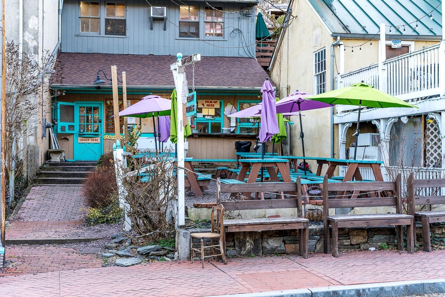 A wooden bench and tables outside a building with a blue door and a sign that says 'ORDER HERE'.