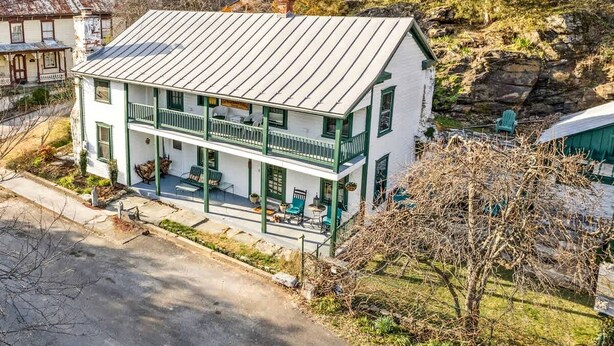 A two-story building with a balcony, a porch with outdoor seating, and a stone foundation.