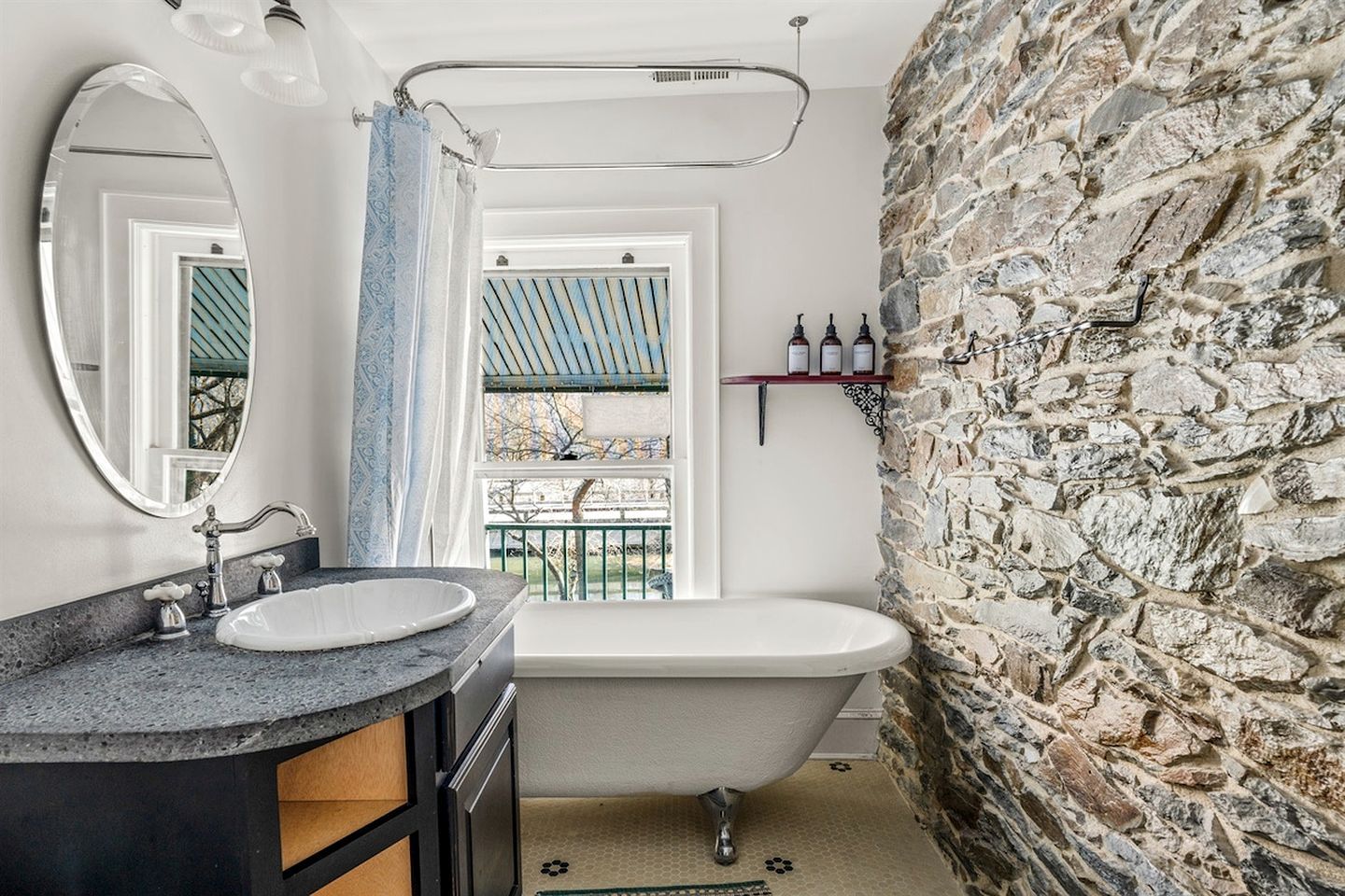 Un baño con una bañera independiente, un espejo grande, un tocador con lavamanos y una pared de piedra.