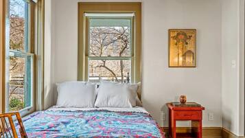 Un dormitorio con una cama grande, una ventana con vistas, una mesita pequeña y una silla.