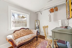 A room with a patterned sofa, a wooden chair, a small table, a mirror, and a drying rack.
