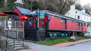 A red building with a black roof, outdoor seating, and a statue of a chef.