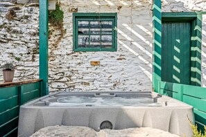 Un bâtiment en pierre avec une porte et une fenêtre vertes, un jacuzzi et un mur en pierre.