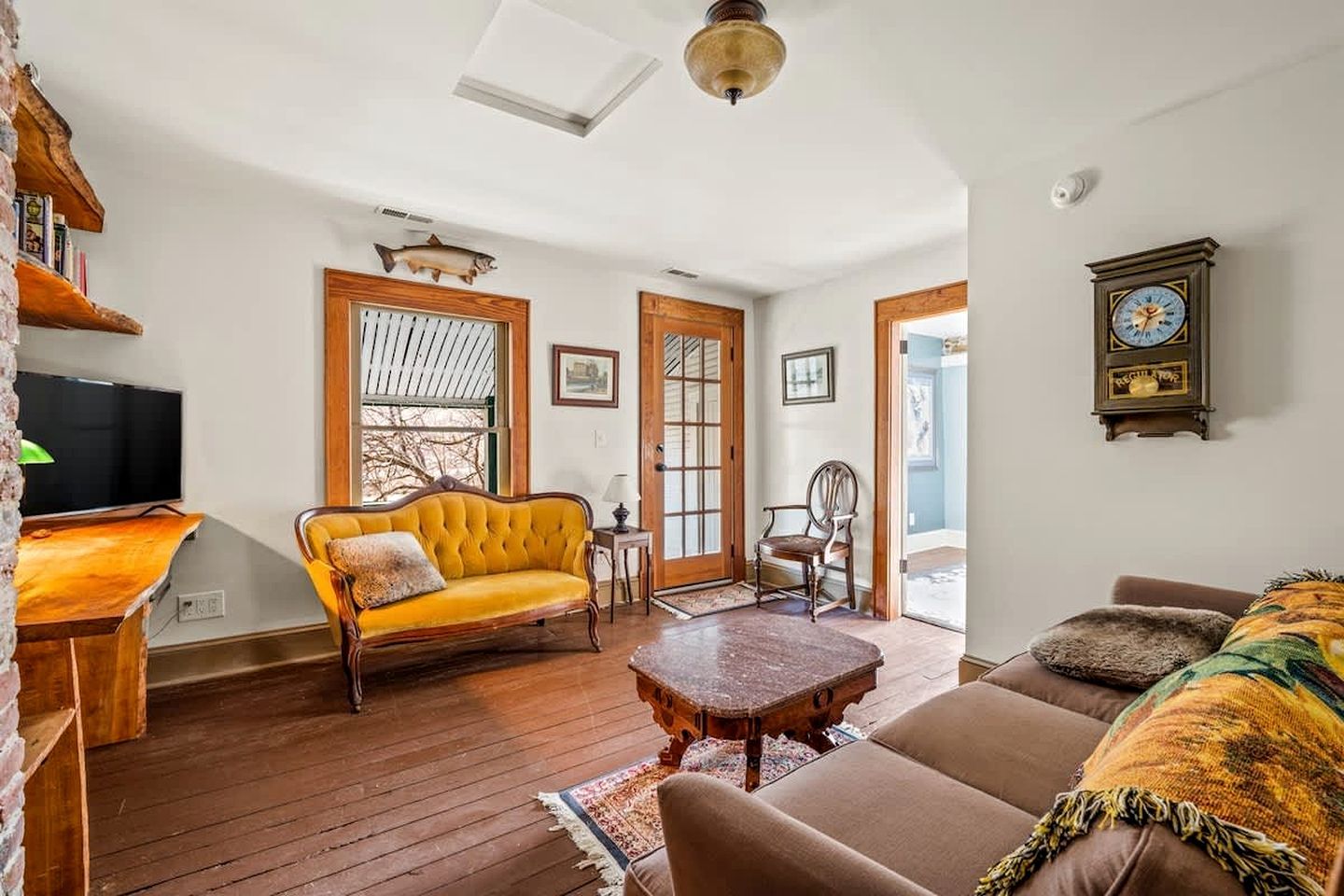 Uma sala de estar com um sofá amarelo, um sofá marrom, uma mesa de centro de madeira e uma televisão sobre um suporte de madeira.