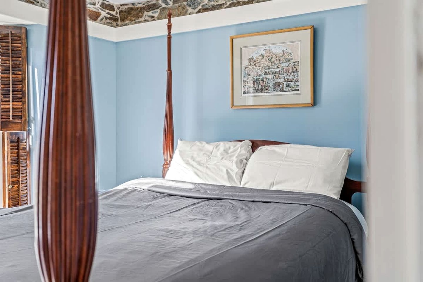 A bedroom with a bed, a framed picture on the wall, and a window with shutters.