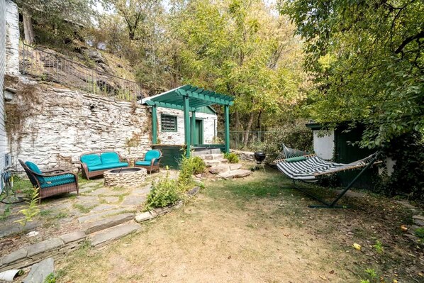 A stone house with a green porch, outdoor seating, and a hammock.