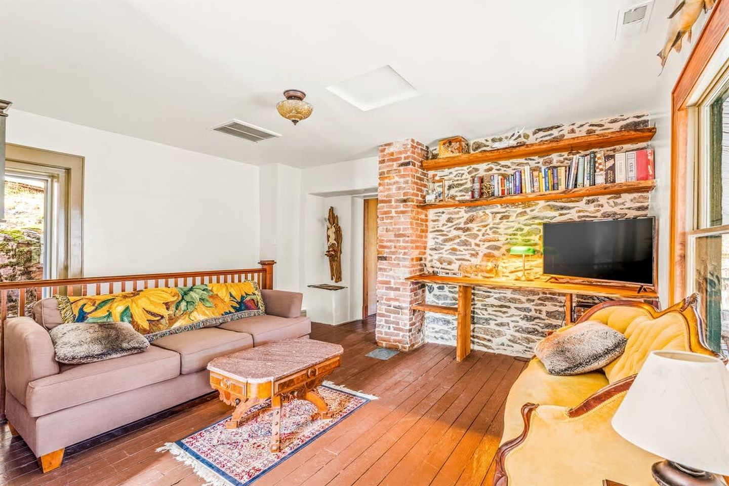 Ein Wohnzimmer mit Sofa, Sessel, Couchtisch und Kaminofen mit Fernseher.