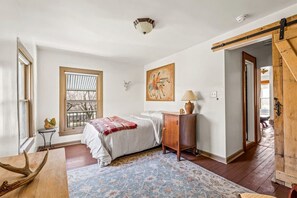 Quarto com cama, janela, quadro, luminária e porta de madeira.