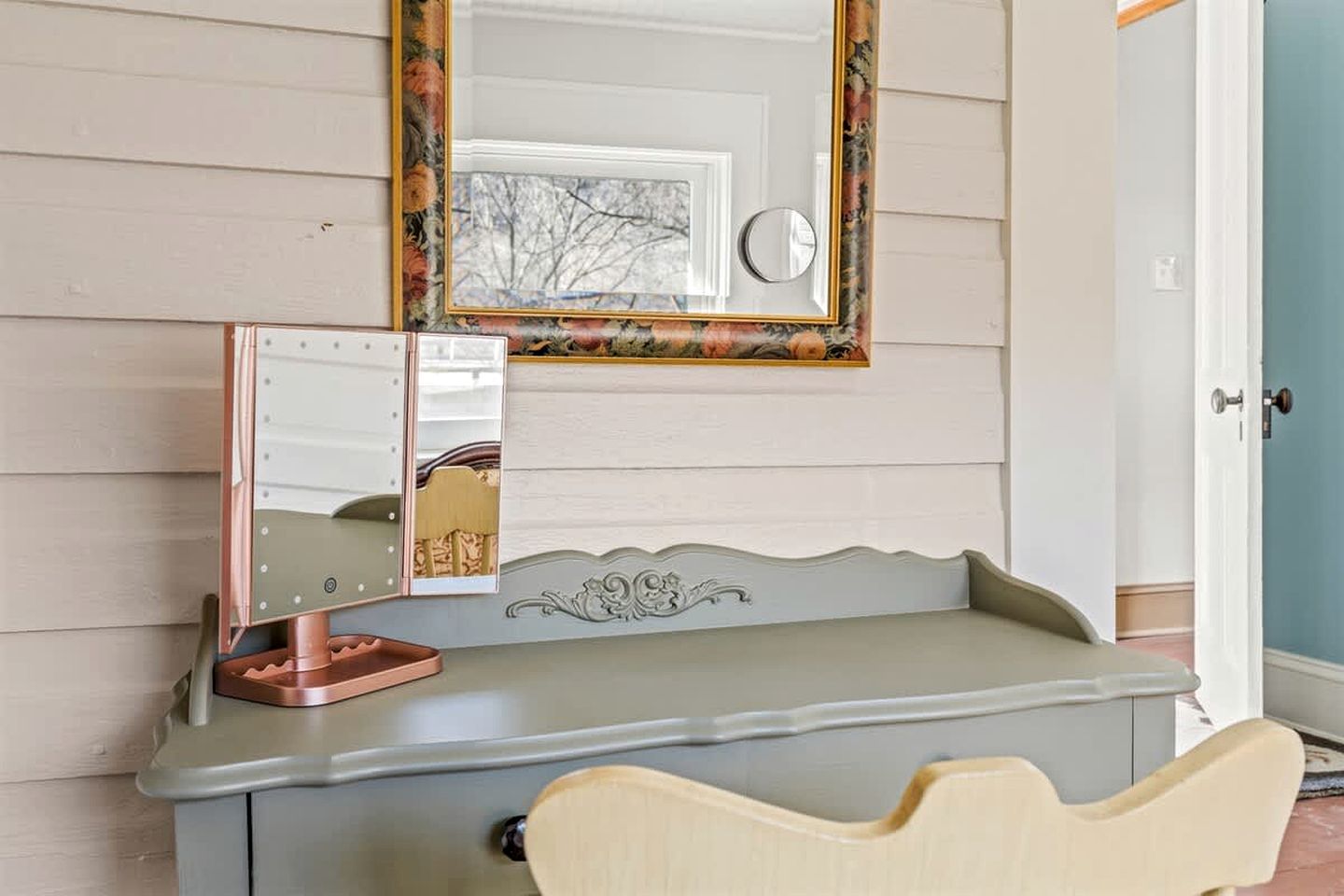 Een kaptafel met spiegel, een kaptafel lamp en een stoel in een kamer met houten wanden.