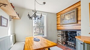 A kitchen with a wooden table, bench, stone fireplace, and a hanging chandelier.