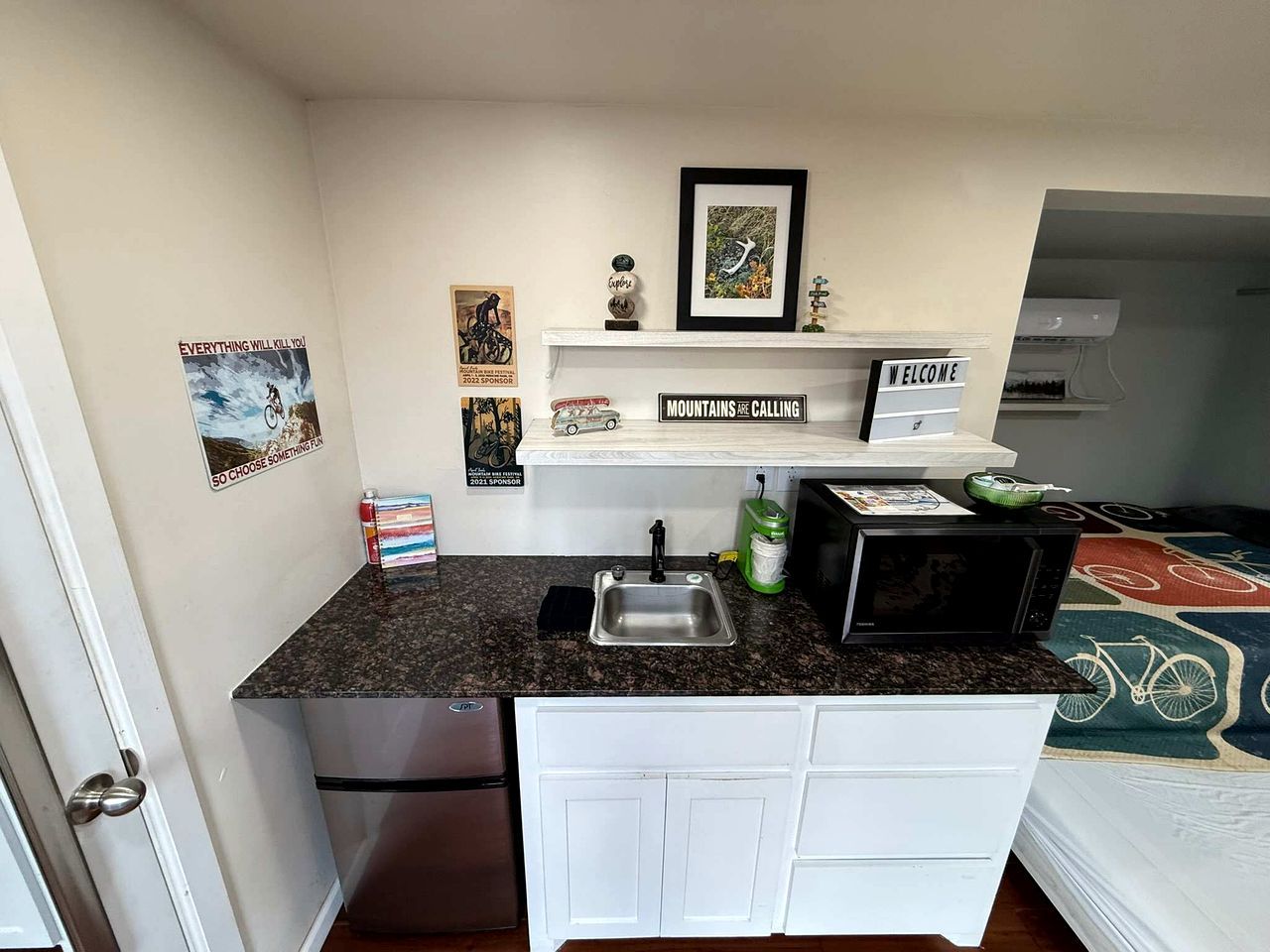 Uma cozinha compacta com pia, micro-ondas e armários brancos.
