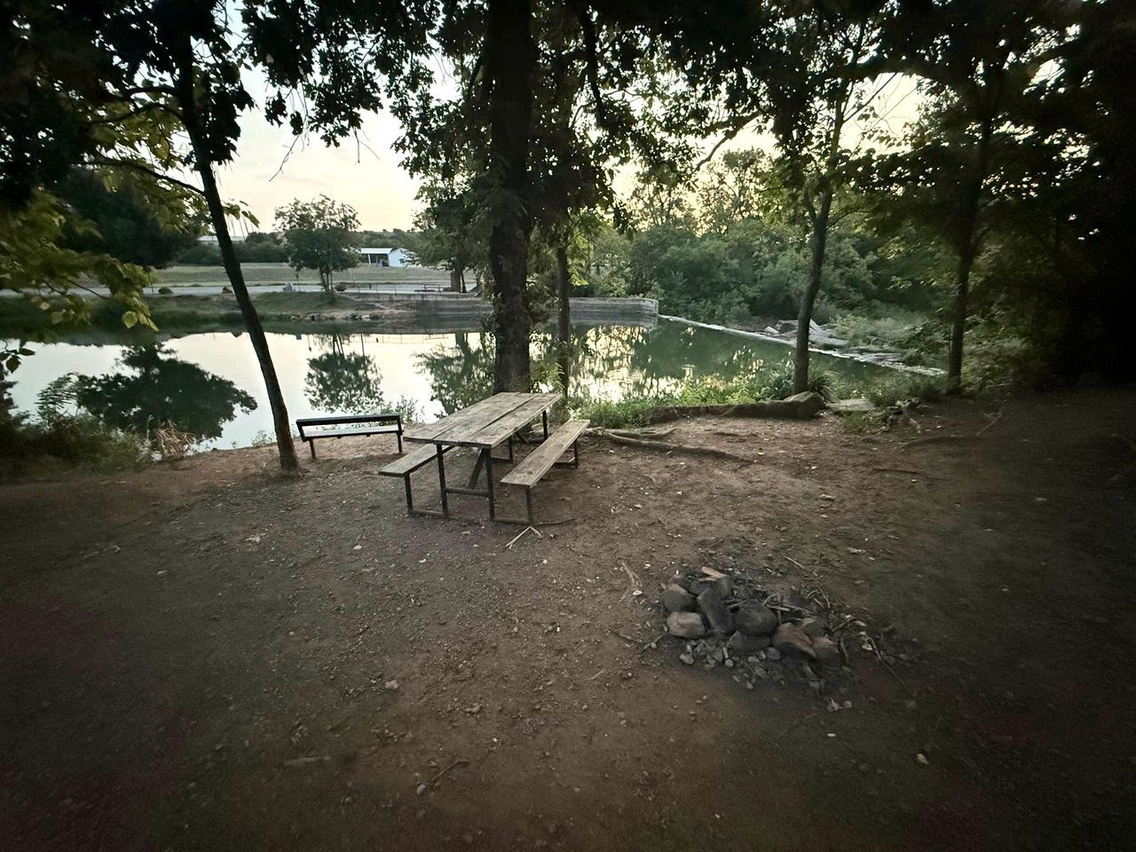Un área de picnic con un banco y una mesa de madera, rodeada de árboles y vistas a un río.