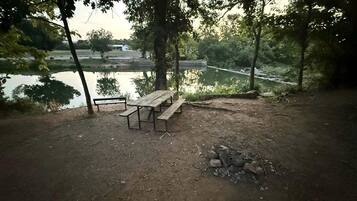 Un área de picnic con un banco y una mesa de madera, rodeada de árboles y vistas a un río.