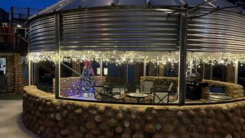 A covered outdoor seating area with stone walls, a Christmas tree, and string lights.