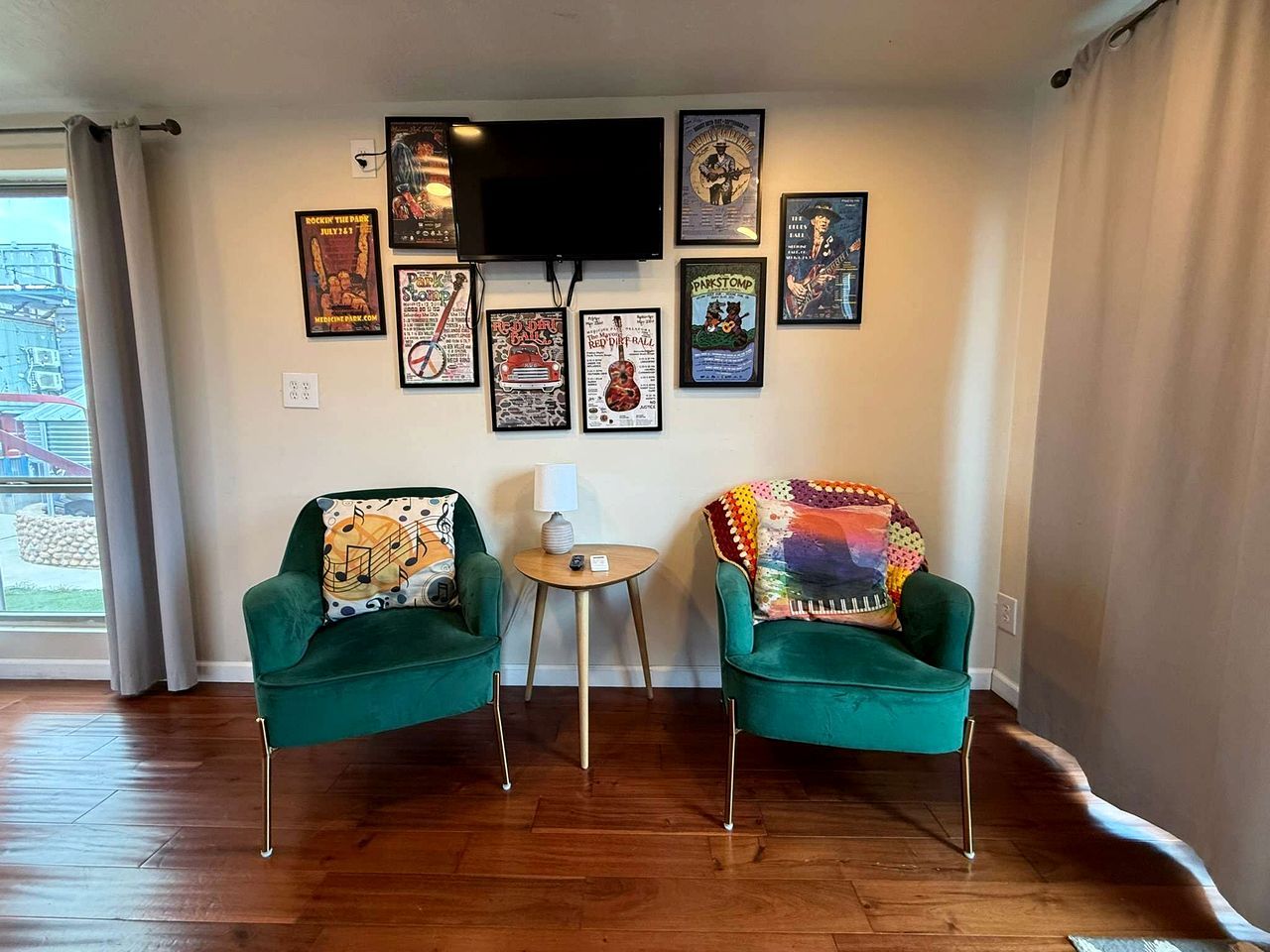 Una sala de estar con dos sillones verdes, una mesita redonda y un televisor montado en la pared.