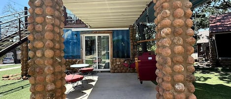 A covered patio area with stone pillars, outdoor seating, and a glass door entrance.