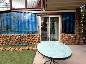 Um pátio com mesa e cadeiras redondas, uma parede de pedra e um mural no prédio.
