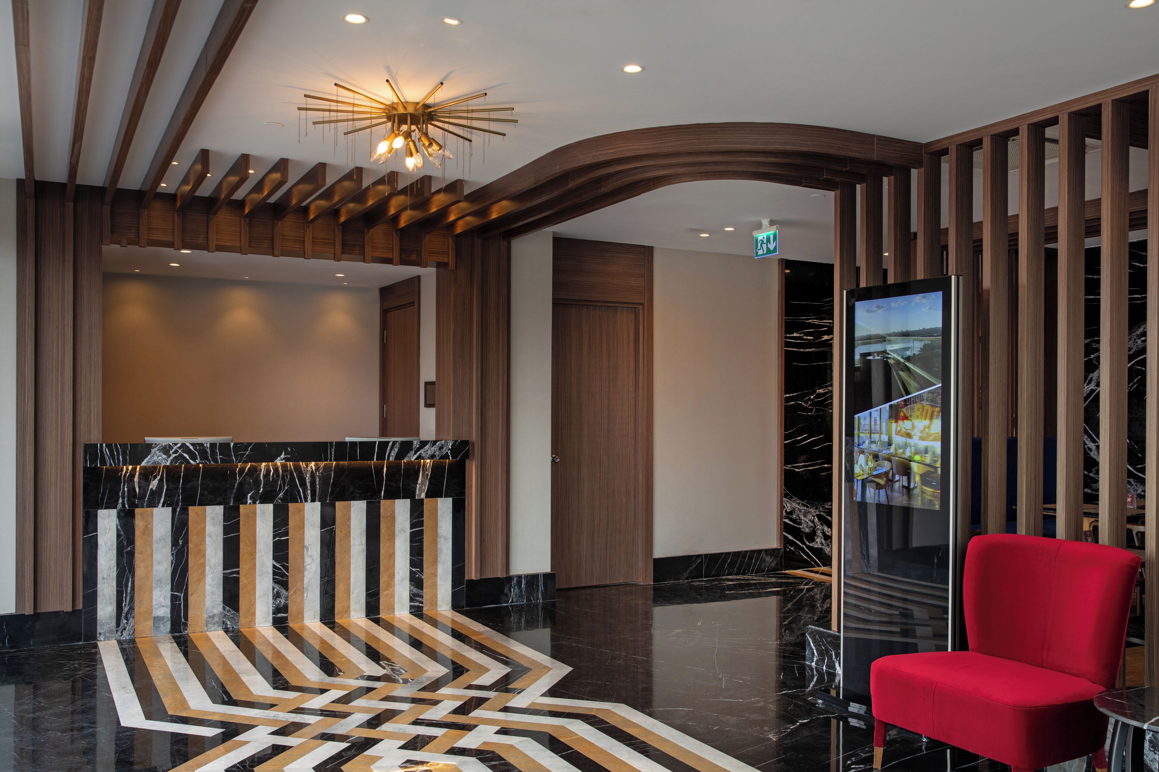 A modern lobby with a reception desk, a red chair, and a unique ceiling design.