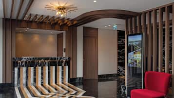 A modern lobby with a reception desk, a red chair, and a unique ceiling design.
