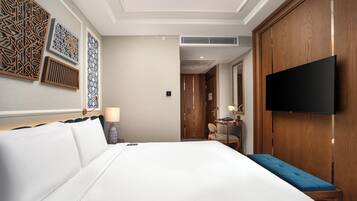 A hotel room with a large bed, a flat-screen TV mounted on the wall, a wooden wardrobe, and decorative wall panels.