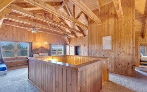 A wooden cabin interior with a central island, a bed with a headboard, and a window with blinds. - Spacious Luxury Log Cabin with Game Room & Panoramic Mountain Views near Pigeon Forge, Tennessee (Sevierville)